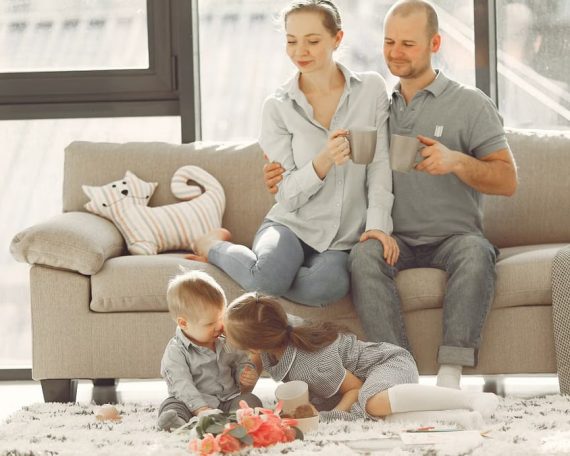 Cheerful family smiling while spending weekend together sitting parents sitting on comfortable sofa while children resting on carpet and playing