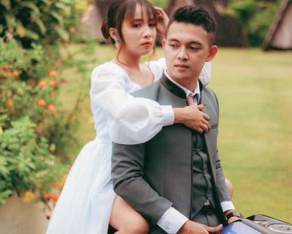 A romantic outdoor scene with an Asian couple in wedding attire, embracing lovingly.