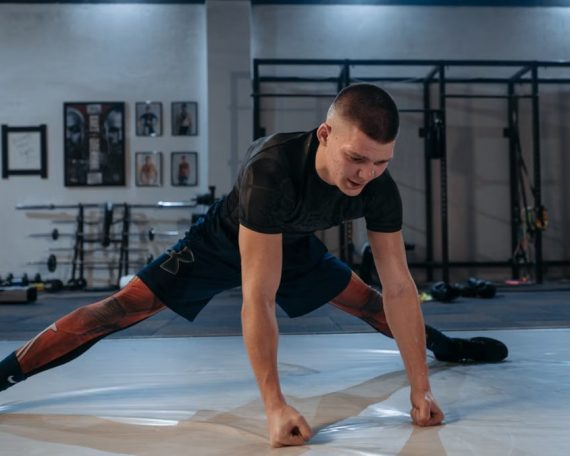 A male athlete stretches intensely in a dimly lit gym environment, preparing for training.
